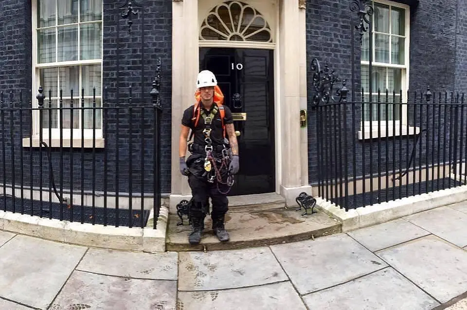 Son of AAA founder Paul Blud in safety gear and helmet window cleaning at the entrance of 10 Downing Street in London.
