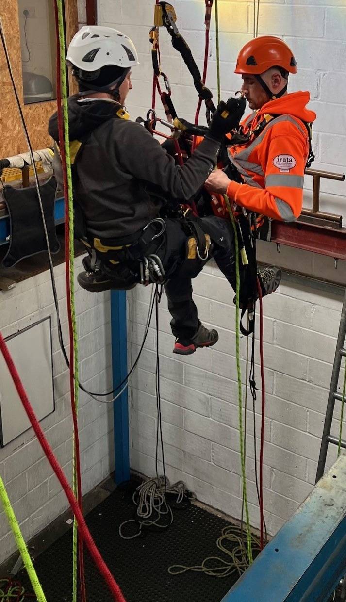 Trainees in safety gear practicing rope access techniques at AAA's IRATA training centre with climbing walls and equipment in the background.
