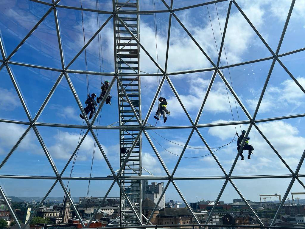 AAA rope technician in safety gear applying Dow Corning 123 Tape on a glazed roof at Victoria Square Shopping Centre, Belfast.