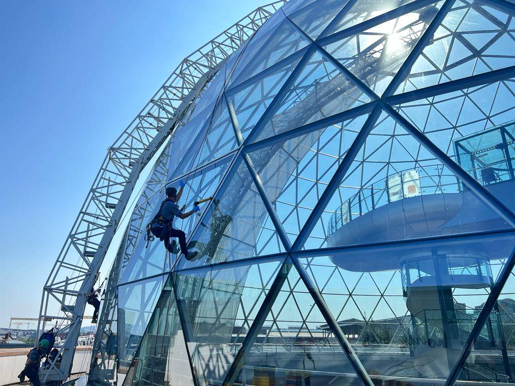AAA rope technician in safety gear applying Dow Corning Tape on a glazed roof at Victoria Square Shopping Centre, Belfast.