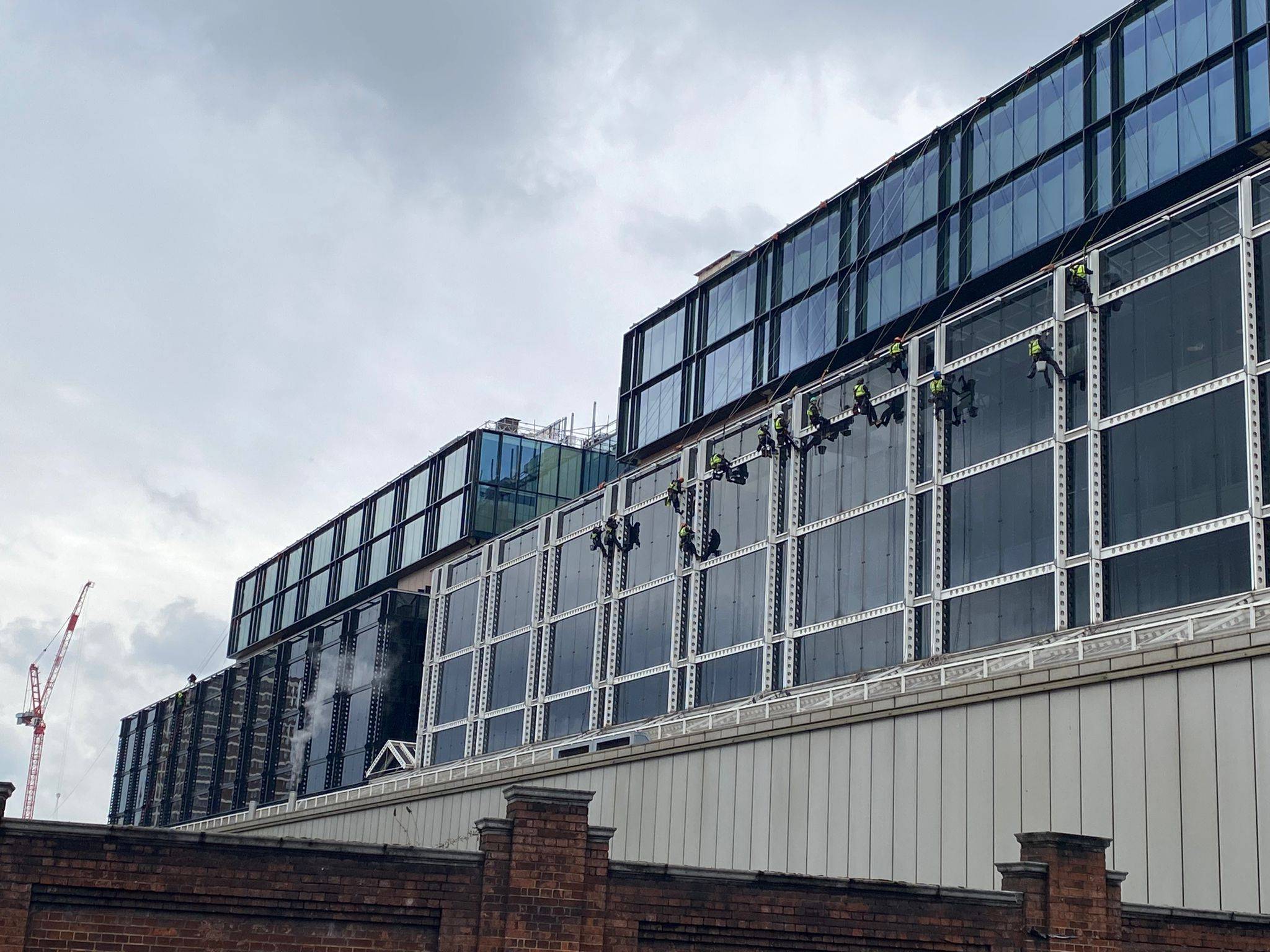 AAA rope technician in safety gear painting the superstructure of 123 Buckingham Palace Road, changing from white to anthracite with London buildings in the background.