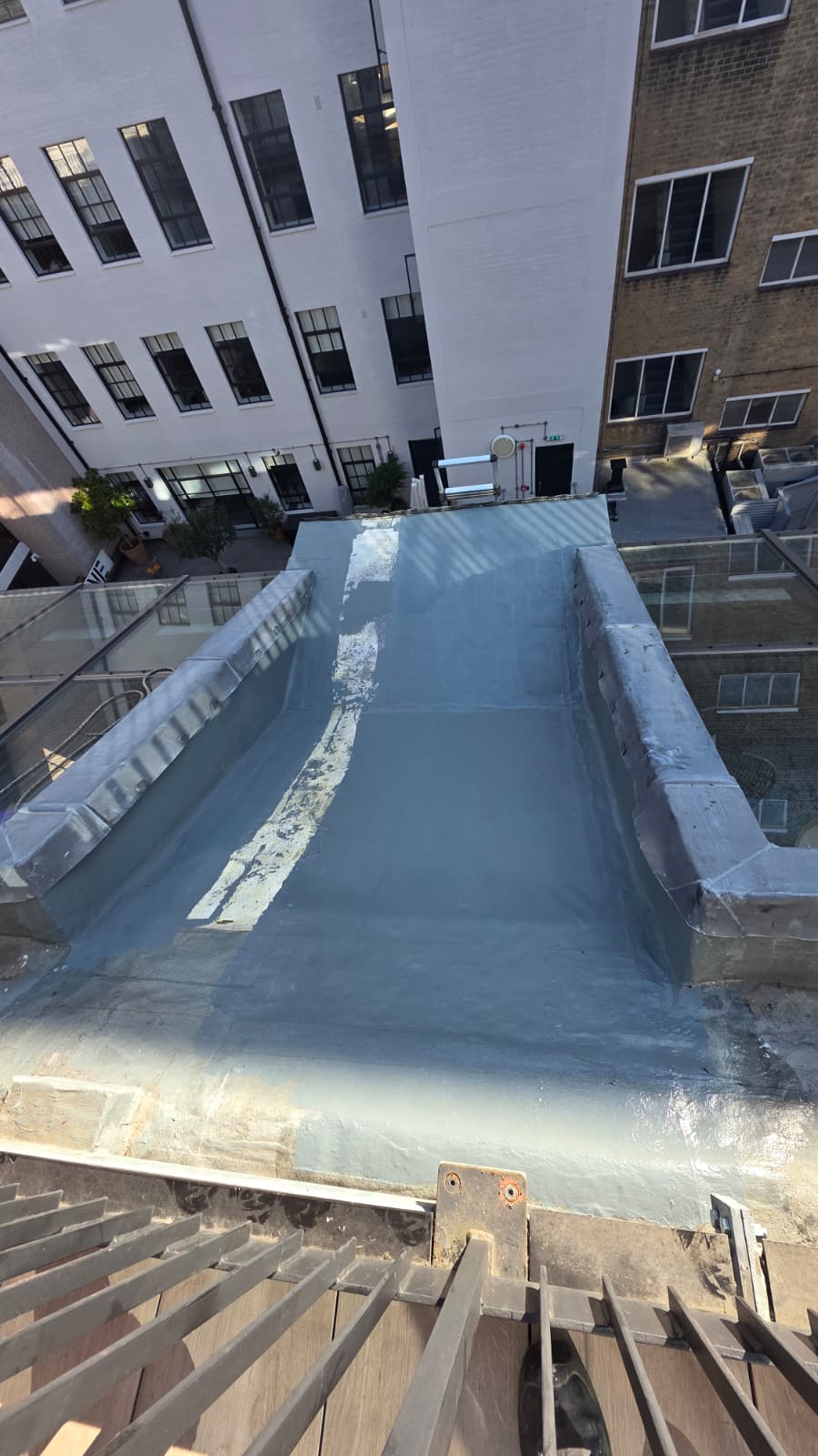 AAA rope technician in safety gear showcasing a finished Tri-Flex roof repair on a sloped roof in a well area, with dormer roof visible.