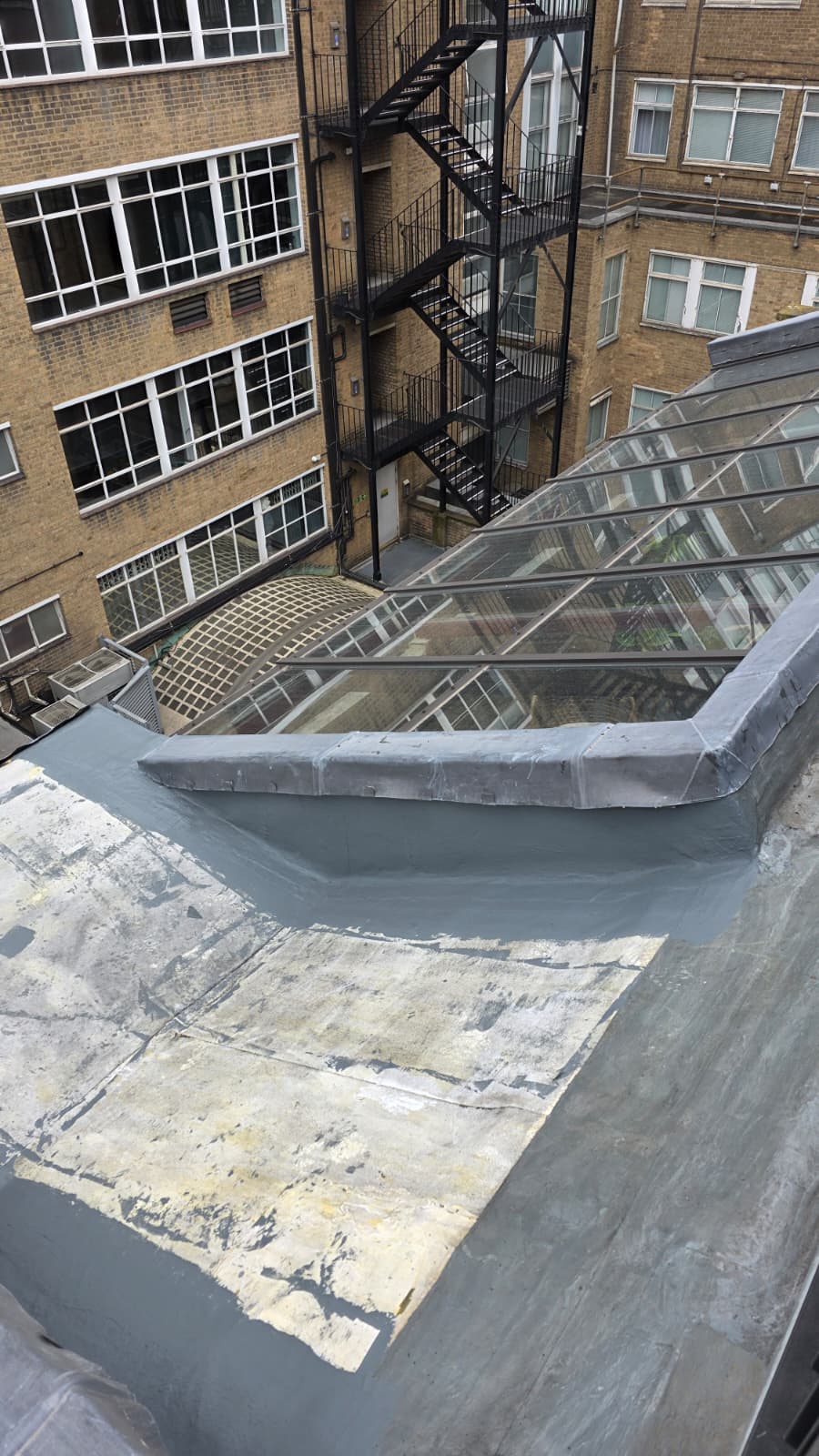 AAA rope technician in safety gear repairing a leaking sloped roof in a well area, with dormer roof and building structure visible.