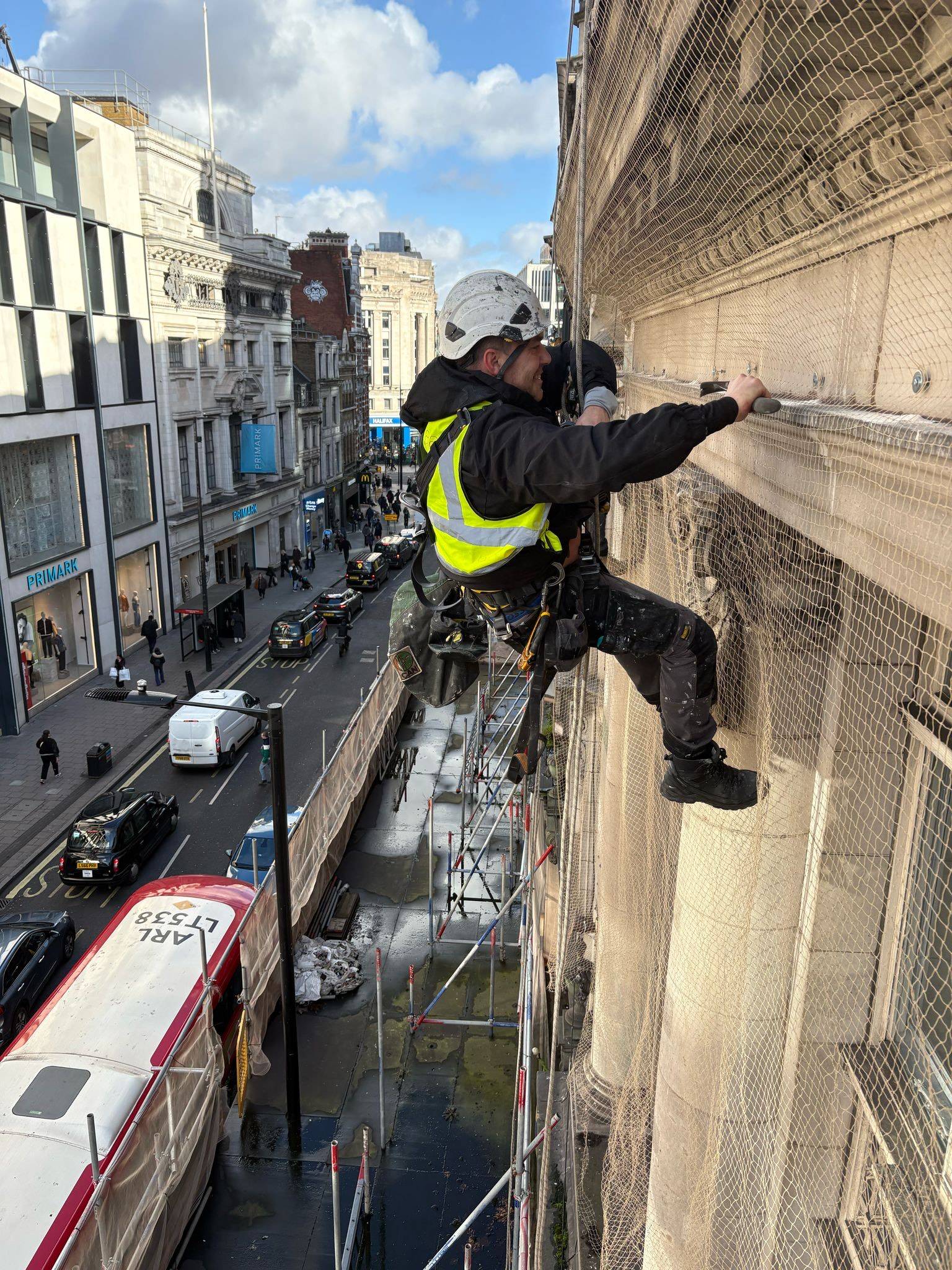 AAA rope technician in safety gear performing emergency stone repairs and installing encapsulation netting on a damaged building facade.