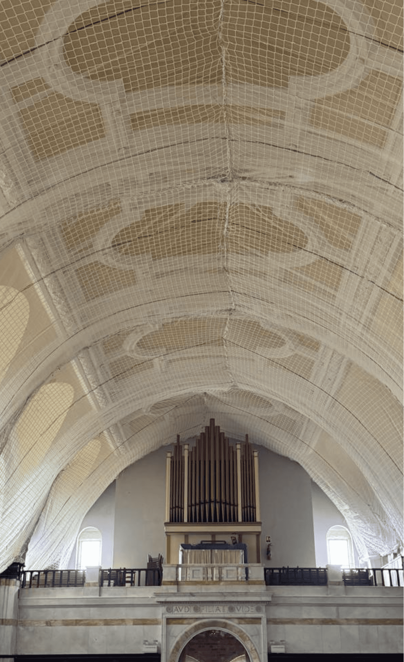 AAA rope technician in safety gear securing the roof with safety nets above a fragile ceiling void at a historic theatre, with ornate architecture visible.