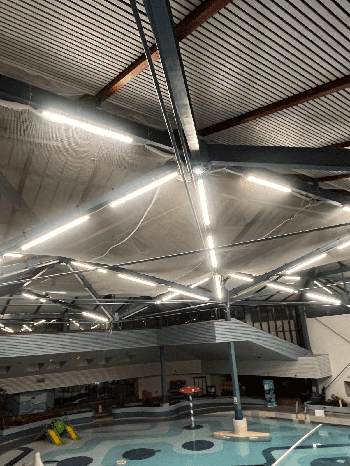 AAA technician in safety gear installing a safety net over a swimming pool, with poolside deck and water visible.