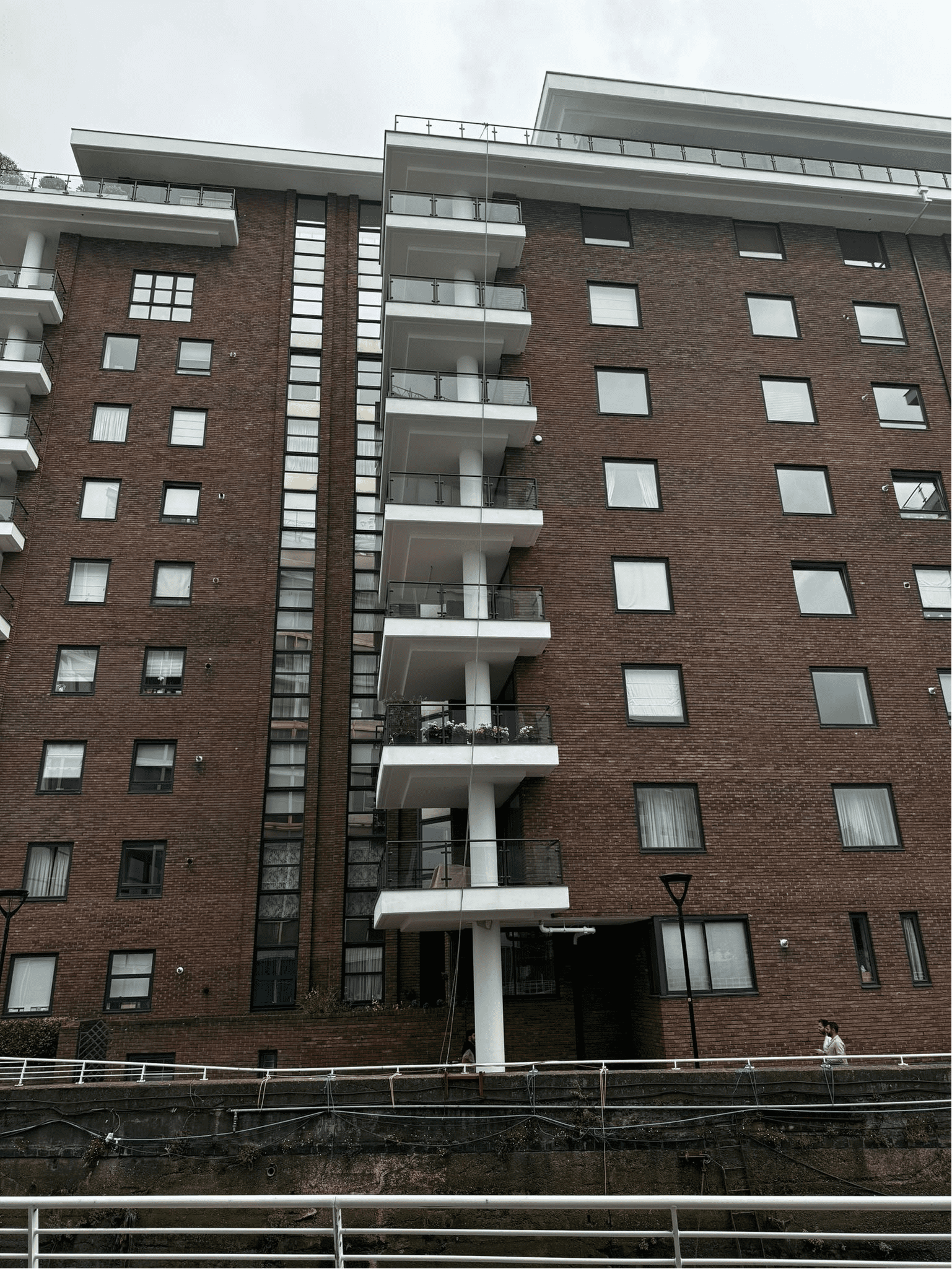 AAA rope technician in safety gear painting and repairing masonry, balconies, and brickwork at Waterside Point with a London river view in the background. completed on time.