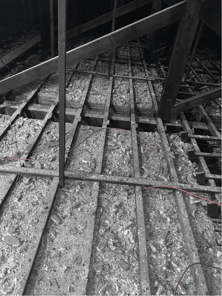 AAA rope technician in safety gear inspecting a fragile ceiling void at a historic theatre, with ornate architecture in the background.