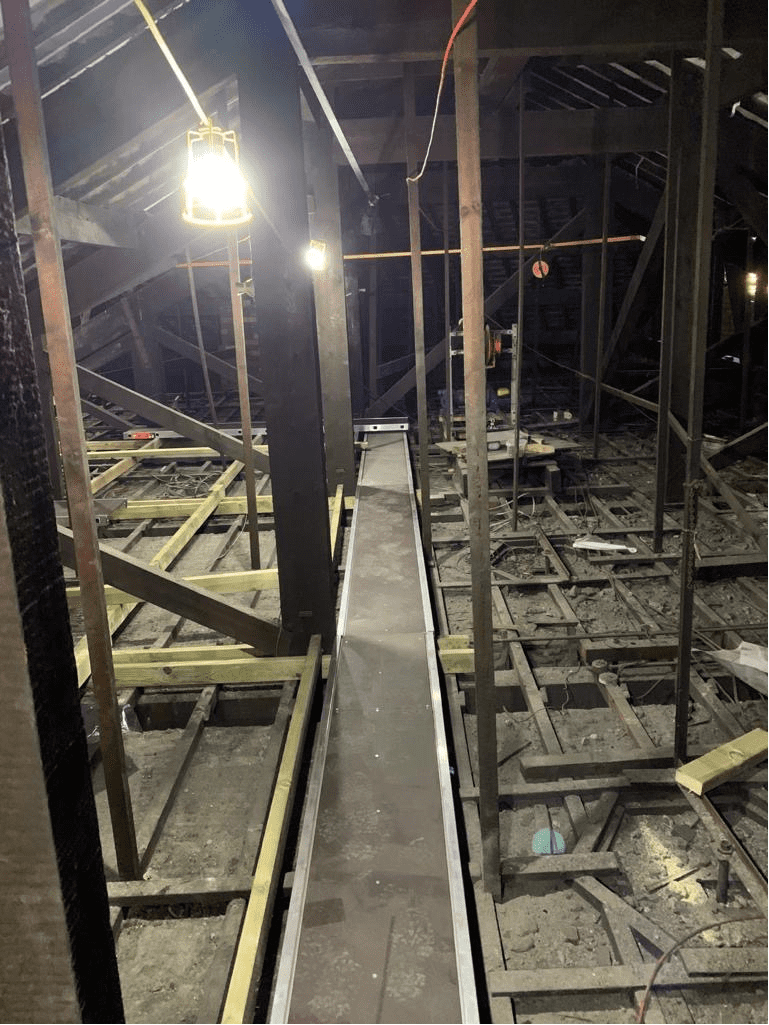 AAA rope technician in safety gear actively inspecting a fragile ceiling void at a historic theatre, with ornate architecture and tools in use.