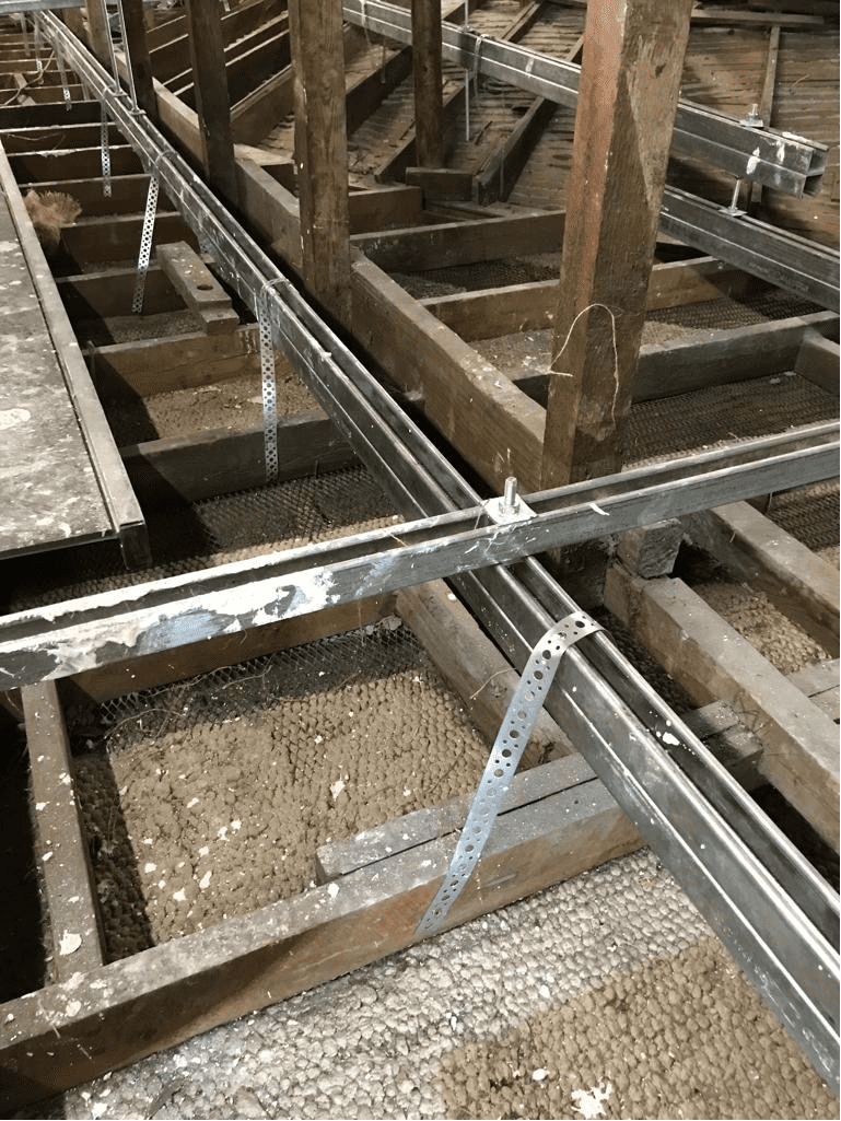 AAA rope technician in safety gear securing the roof above a fragile ceiling void at a historic theatre, with ornate architecture and tools visible.